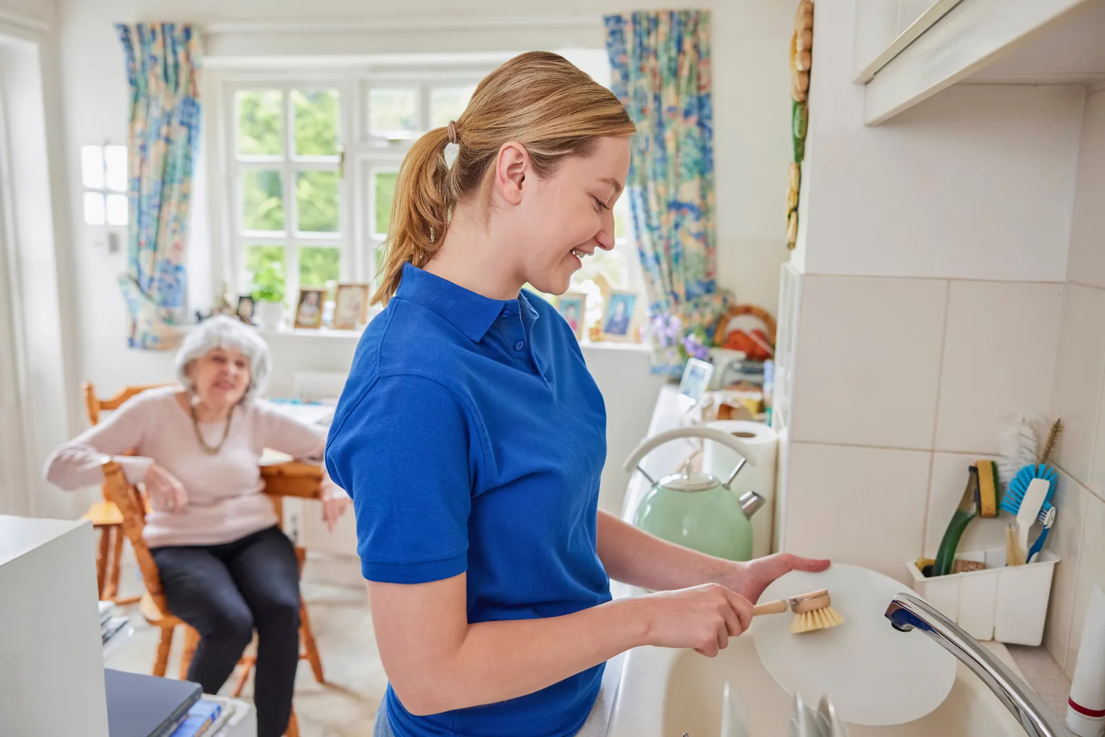 Carer washing up while chatting to her client in the kitchen
