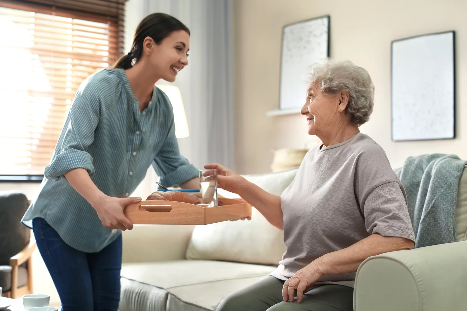 Care worker bringing a meal tray to an elderly woman in her lounge